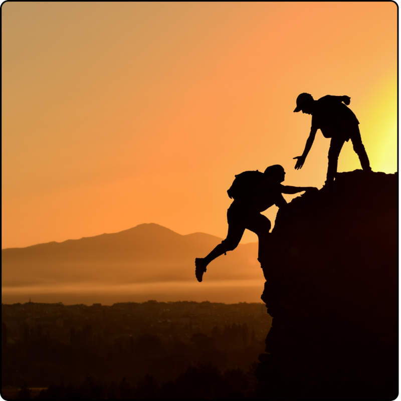 A person lending a hand to another person trying to reach the top of a rock.