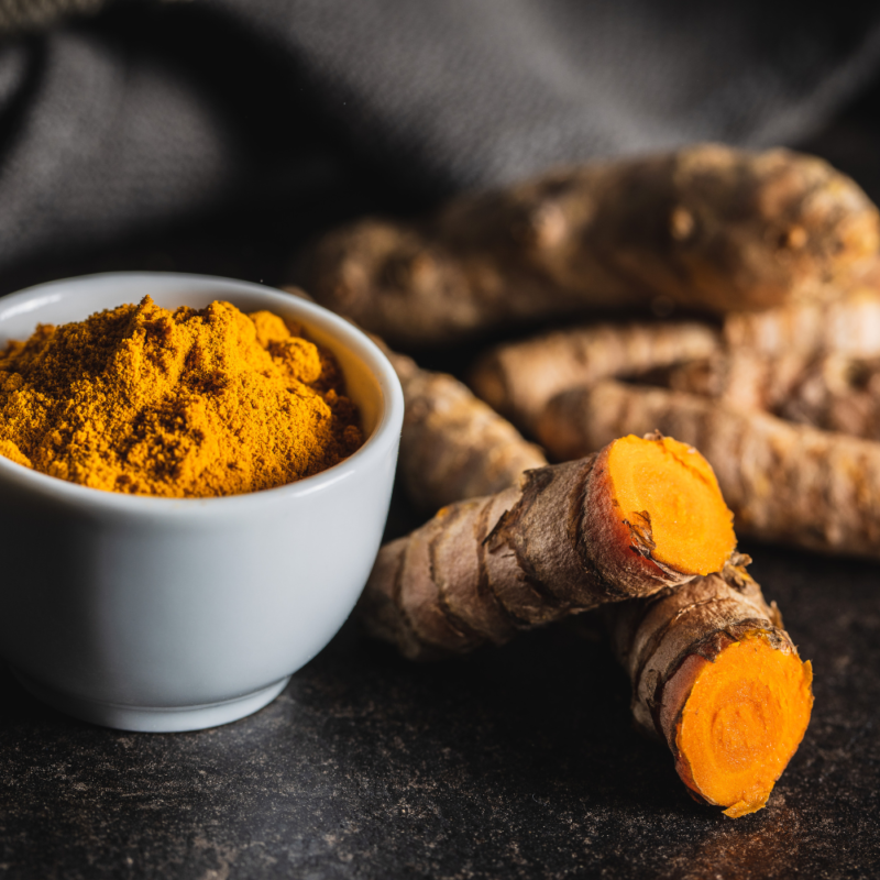 A bowl filled with grounded turmeric and fresh turmeric root.